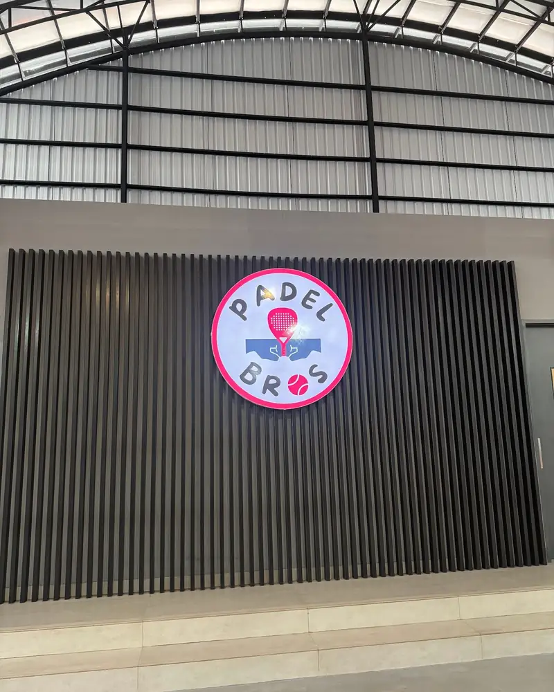 The round Padel Bros badge on the slatted lounge wall